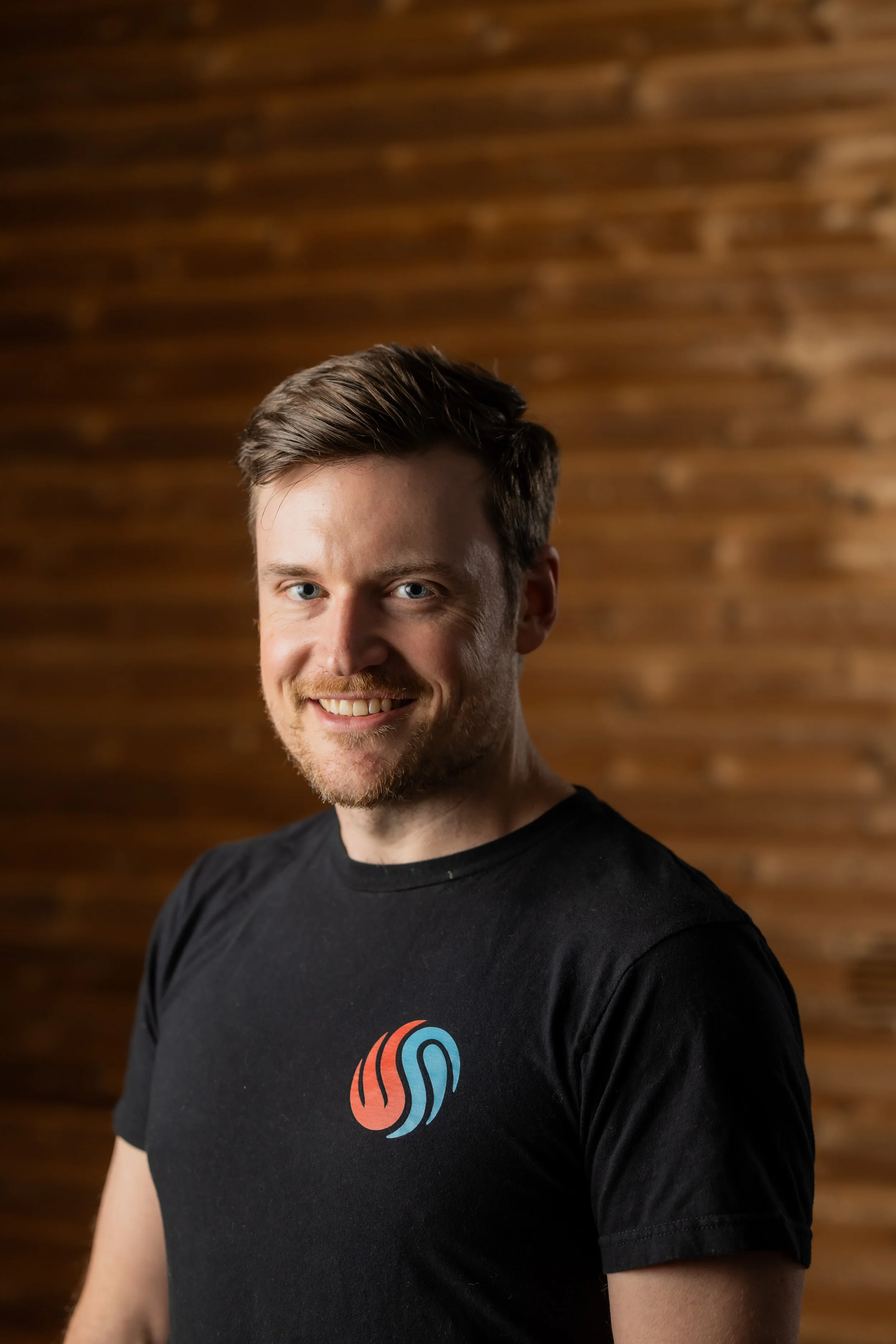 Chillfire Sauna Company team member smiling in front of a wooden background, representing our hands-on sauna craftsmanship and friendly team.