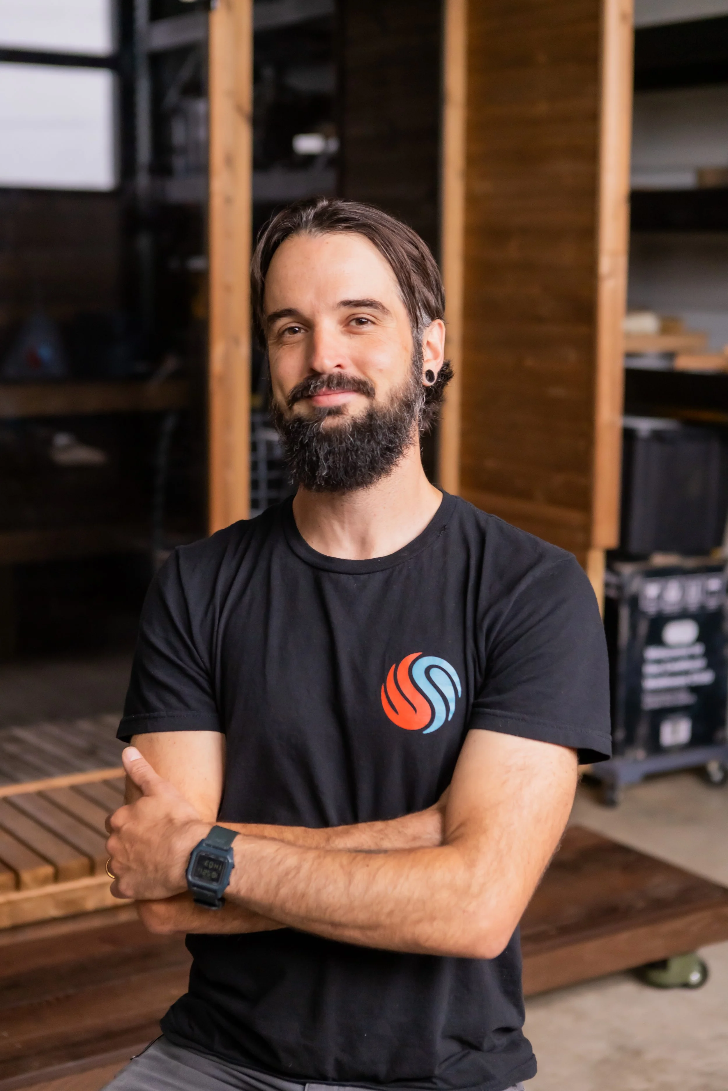 Chillfire Sauna Company team member standing with arms crossed inside a wooden sauna workshop, representing our hands-on craftsmanship and custom sauna construction.